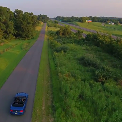 Thumbnail of a drone video showing a Ford Mustang driving on an empty stretch of country road.